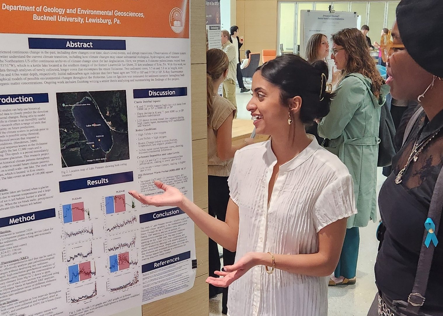 A student gesturing to a poster, explaining the contents to a person listening.